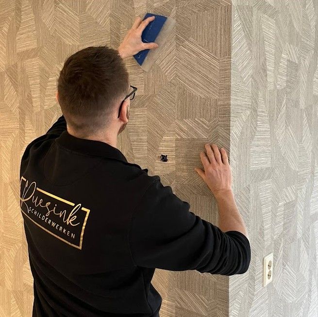 Schilder in een zwarte Ruesink-trui strijkt behang met een geometrisch patroon glad